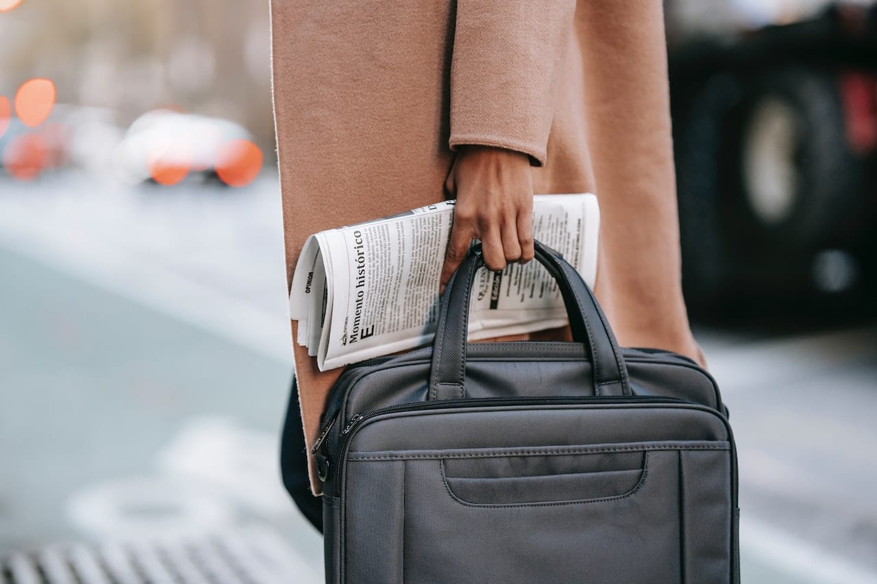 person in trench coat holding a newspaper and a laptop bag